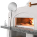 Fresh pizza being cooked in a Palazzetti Antille Complete Outdoor BBQ Kitchen with Wood Fired Oven with a pizza paddle leant on it